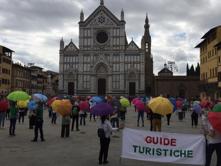 Guide in piazza Santa Croce senza turisti, con ombrelli e manuali d’arte